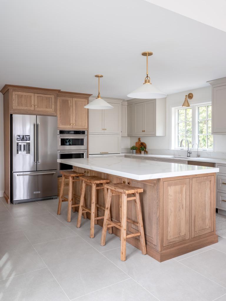 Bogert Home kitchen — white oak island and counter stools beside a stainless steel refrigerator and built-in double wall ovens